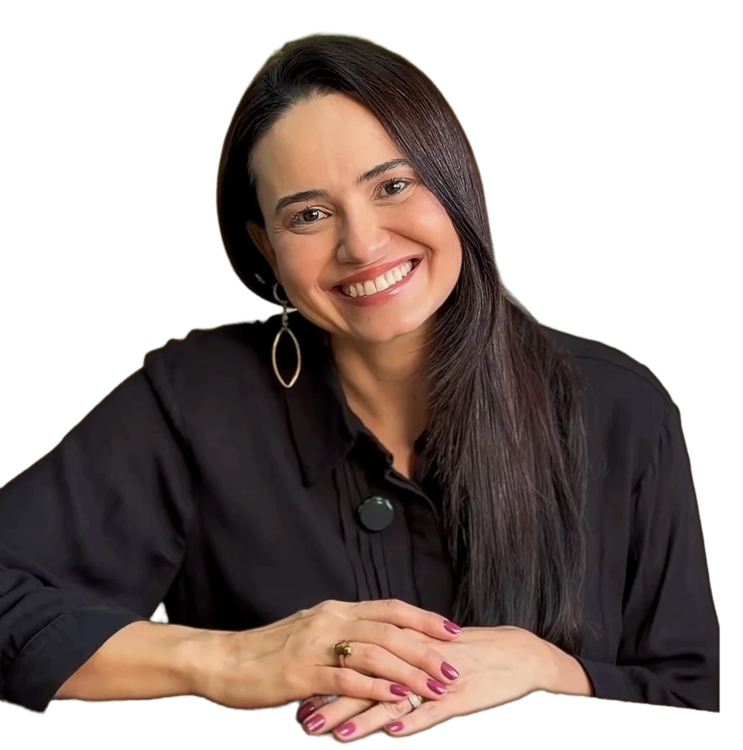 Dra. Luana Menezes sorrindo, de camisa preta, com as mãos cruzadas sobre a mesa do consultório